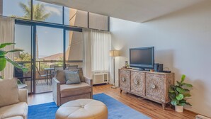 Ein modernes Wohnzimmer mit großem Fernseher, bequemen Sitzmöglichkeiten, einem Balkon mit Aussicht und einem dekorativen Schrank.