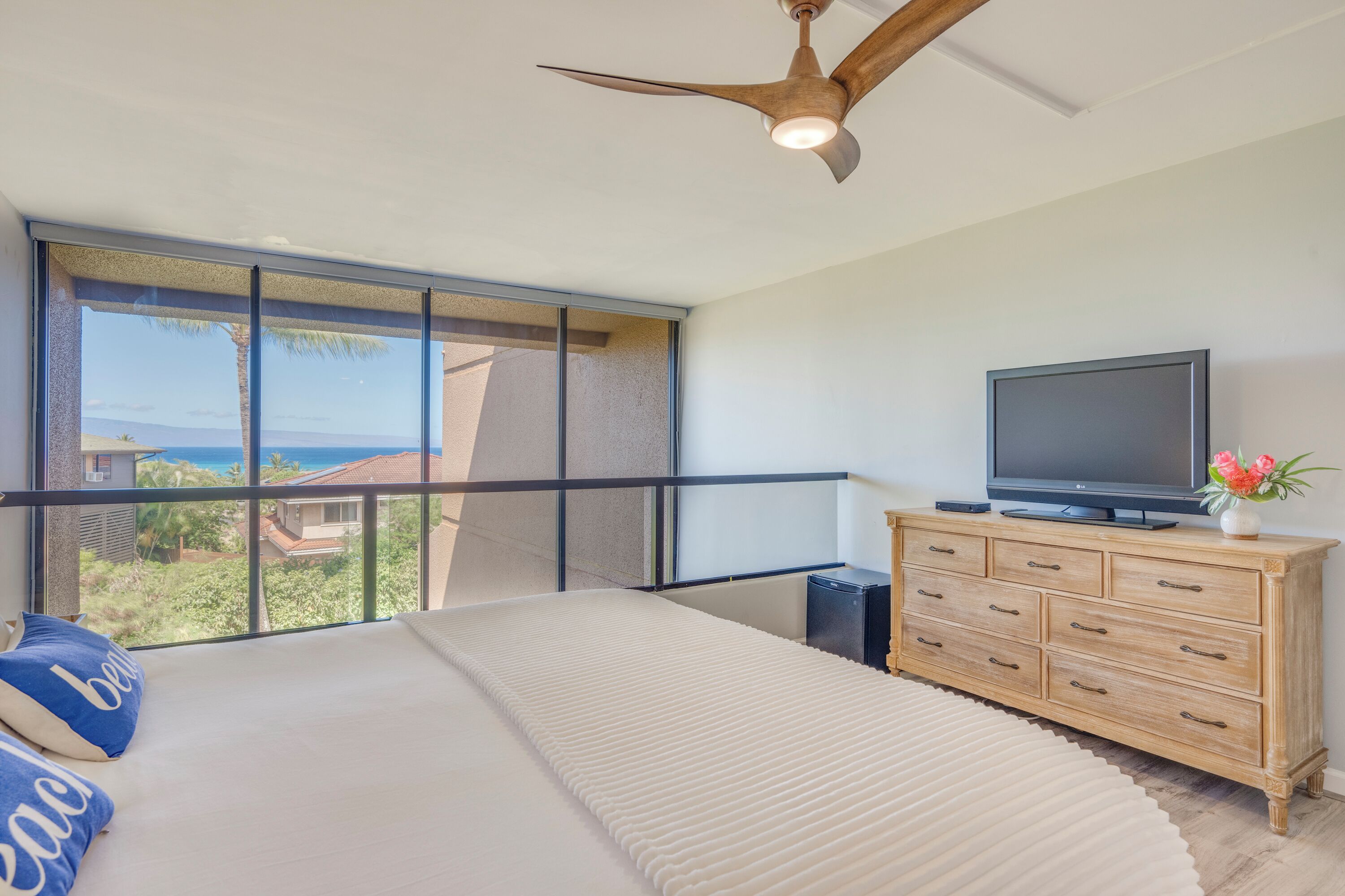Ein Schlafzimmer mit einem großen Bett, einer Holzkommode, einem Fernseher und einem Balkon mit Meerblick.
