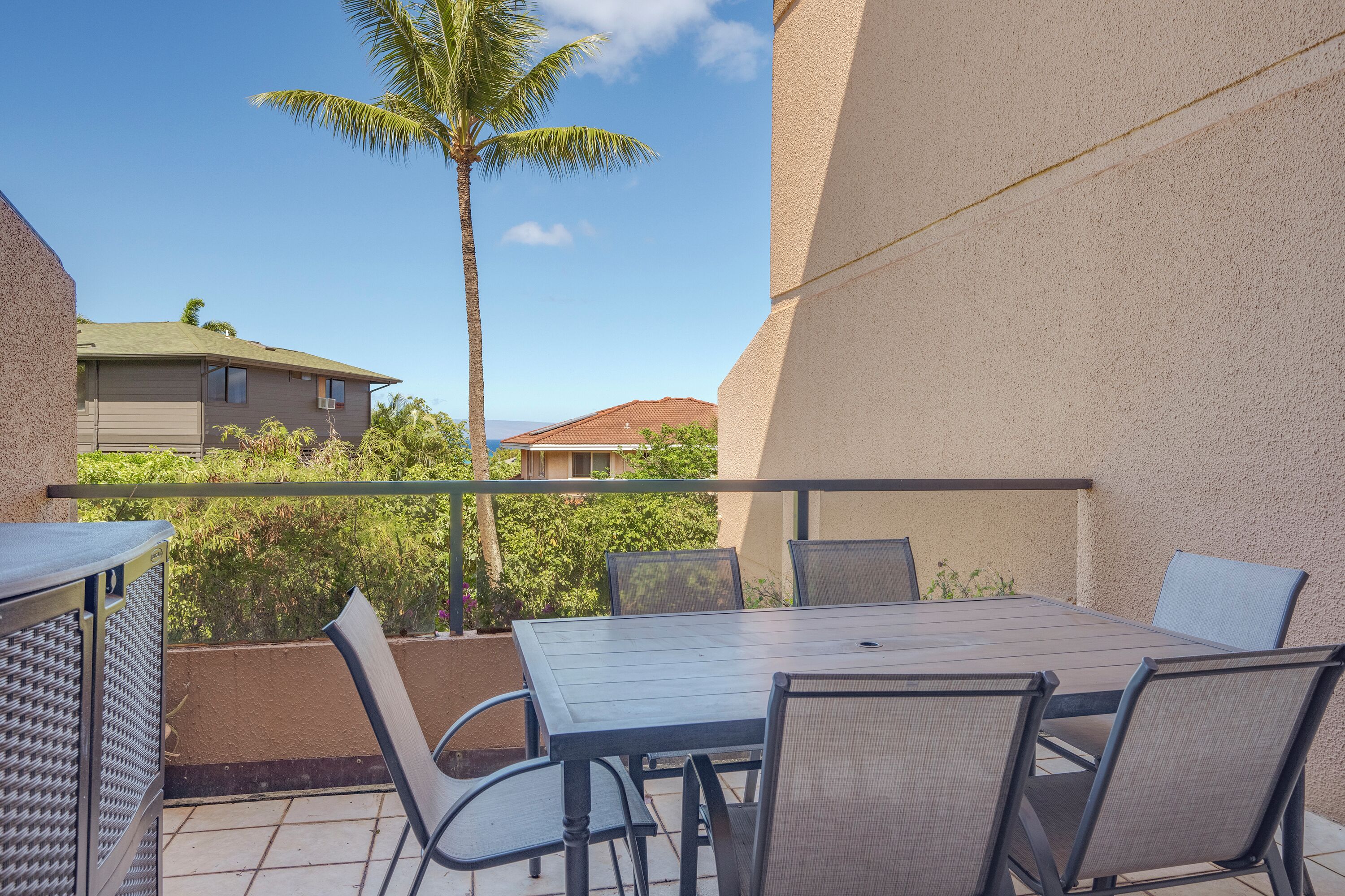 A balcony with a table and chairs, a palm tree, and a view of neighboring buildings.