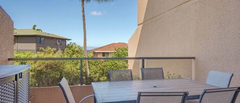 A balcony with a table and chairs, a palm tree, and a view of neighboring buildings.