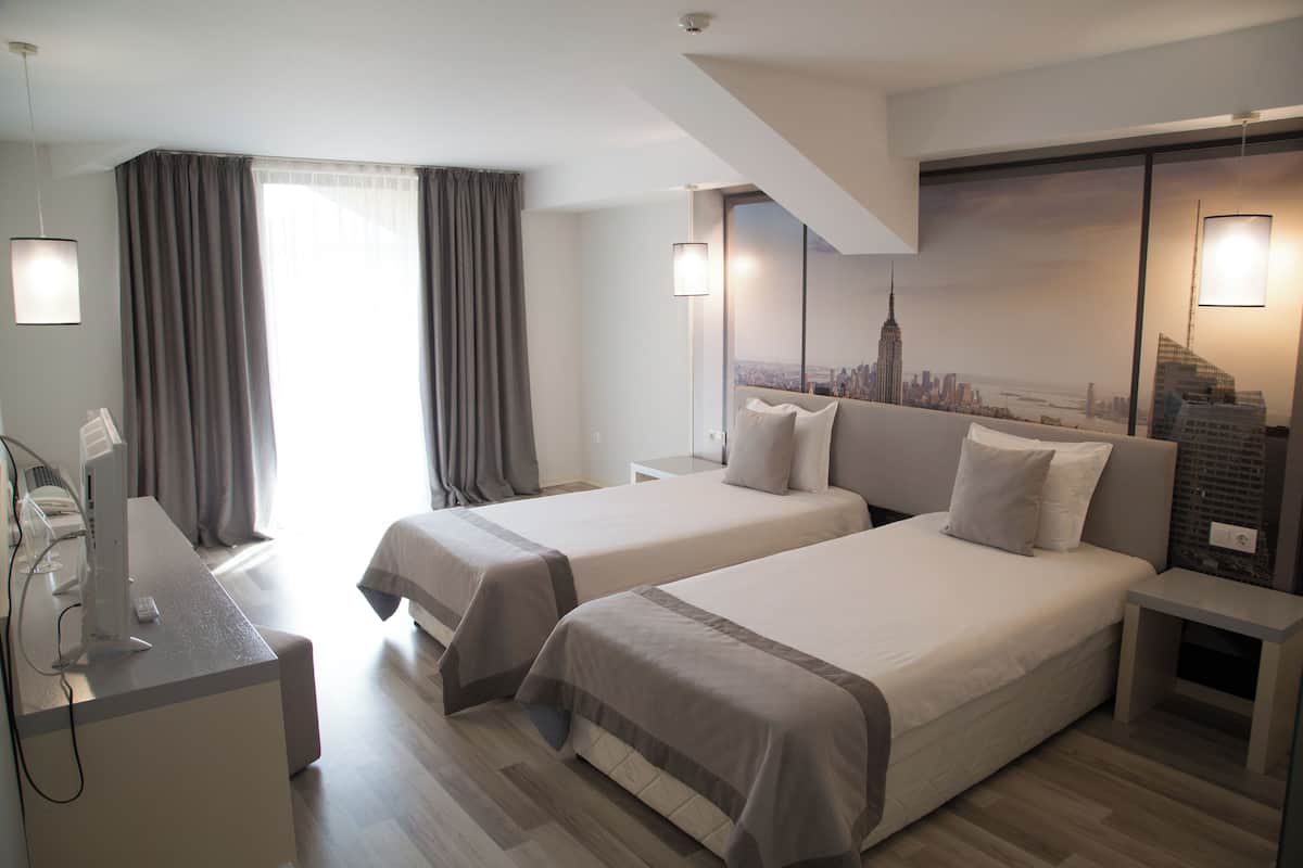 A hotel room with two beds, a desk, and a cityscape mural on the wall.
