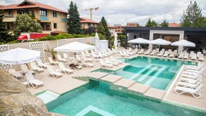 A swimming pool area with lounge chairs and umbrellas, surrounded by buildings and trees.