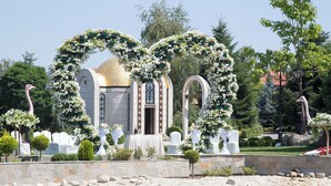A building with a dome, surrounded by a garden with white flowers and trees.