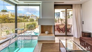 A modern living room with a glass pool, clear chairs, a fireplace, and a view of the city. - A2 -  luxury house with pool (Porto Heli)