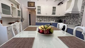 Une cuisine moderne avec des meubles blancs, un îlot central agrémenté d’un panier de fruits et un crédence décorée.
