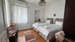 Une chambre d’hôtel avec deux lits, un plancher en bois, un tapis à rayures, une petite table avec une lampe et une fenêtre avec des rideaux.
