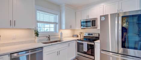 A modern kitchen with white cabinetry, stainless steel appliances, and a window with blinds.