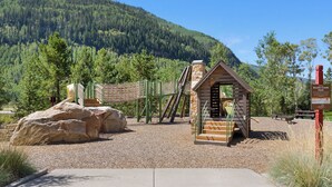 A playground with a rope bridge, a wooden playhouse, and a large rock. - Charming and Upgraded 3 Bedroom Mountain Townhome by Gorecreek Rentals (Vail)