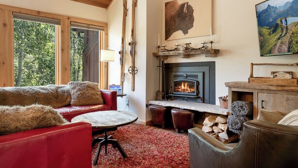 A cozy living room with a fireplace, a red sofa, a round coffee table, and a painting of a mountain landscape. - Charming and Upgraded 3 Bedroom Mountain Townhome by Gorecreek Rentals (Vail)