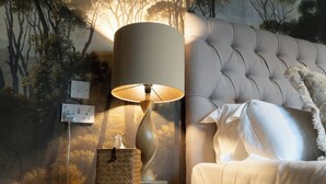 Ein Schlafzimmer mit einer gepolsterten Kopfteile, einer Nachttischlampe, einem Nachttisch mit Lampe und Korb sowie einer Wandsteckdose.