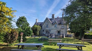 Ein Steinhaus mit Garten und einer Terrasse, auf der Picknicktische stehen.