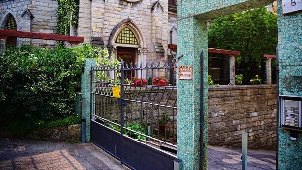 A gated entrance to a building with a stone facade, a sign indicating 'Condominio Valassina', and a small garden area with potted plants. - Coral Blue by Wonderful Italy (Bellagio)