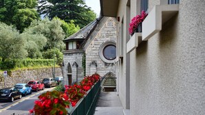 A stone building with a round window and a balcony with red flowers. - Coral Blue by Wonderful Italy (Bellagio)