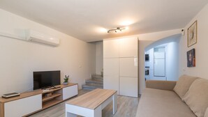 Uma sala de estar moderna com televisão, mesa de madeira, sofá e escada que leva a uma cozinha.