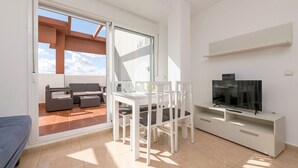 A modern living room with a TV, white furniture, and a sliding glass door leading to an outdoor seating area. - Atico Santa Fe in El Puerto de Santa Maria (El Puerto de Santa Maria)