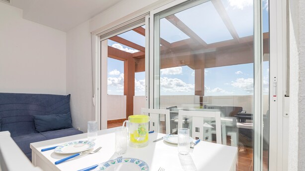 A dining area with a table set for two, a sofa, and a view through a glass door to the outside. - Atico Santa Fe in El Puerto de Santa Maria (El Puerto de Santa Maria)