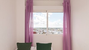 A room with a bed, two pillows, and a window with purple curtains. - Atico Santa Fe in El Puerto de Santa Maria (El Puerto de Santa Maria)