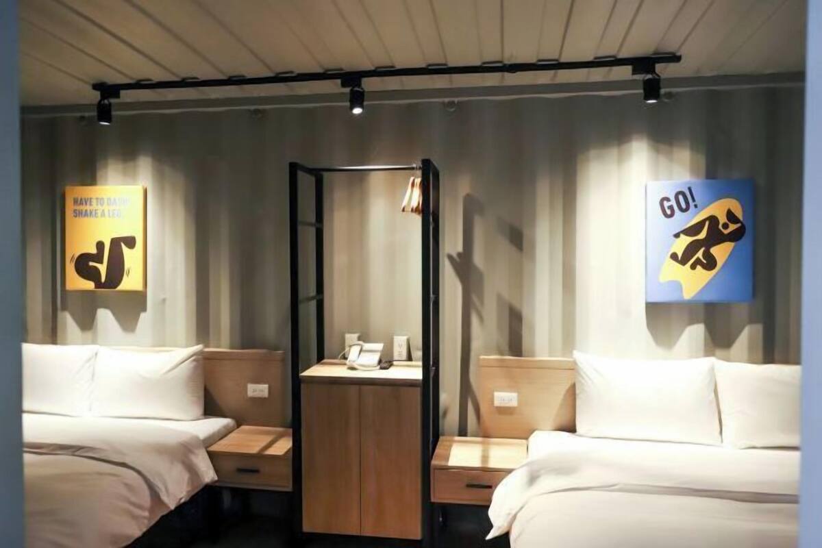 A hotel room with two beds, a small table, and a wardrobe. There are motivational posters on the walls.