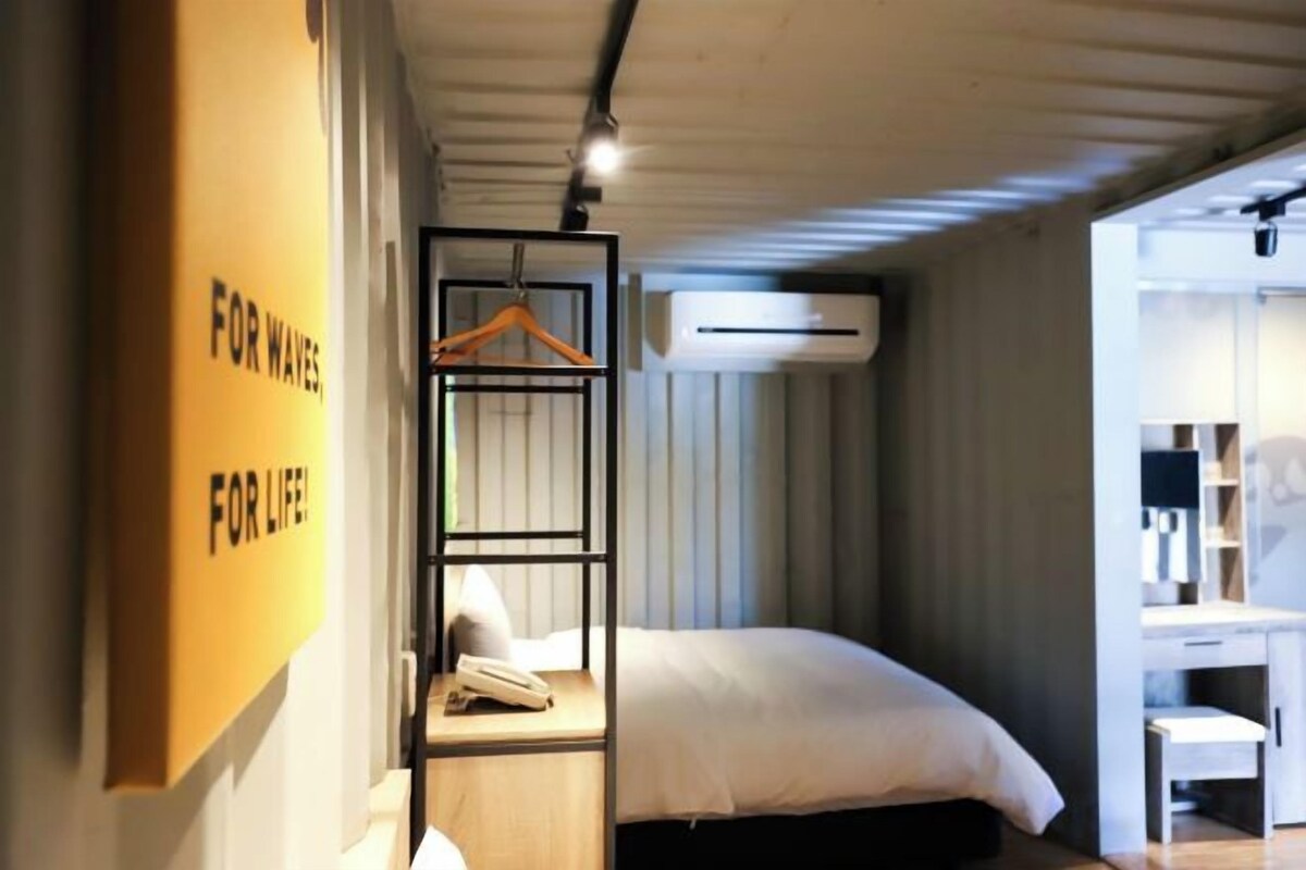 A hotel room with a bed, a hanging shelf, and a desk.