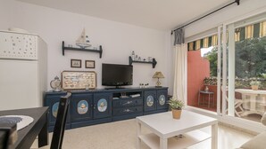 Een woonkamer met een televisie, een blauwe kast met decoratieve objecten, een witte tafel en een bank.