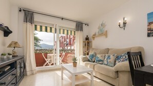 Een woonkamer met een bank, een salontafel en een eettafel. Er is een balkon met uitzicht op gebouwen en bergen.