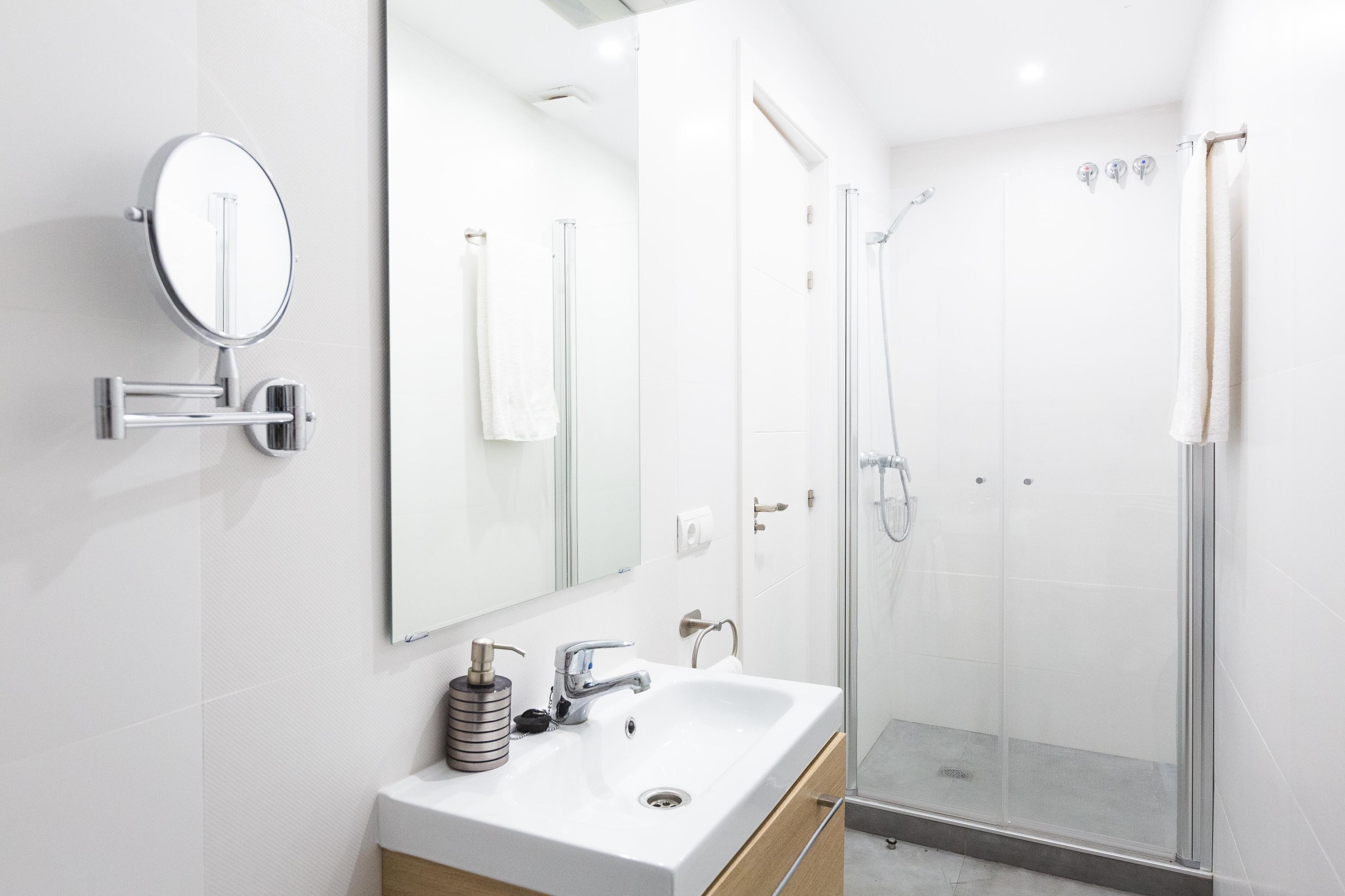 A modern bathroom with a white sink, a mirror, a handheld showerhead, and a glass-enclosed shower.