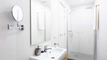 A modern bathroom with a white sink, a mirror, a handheld showerhead, and a glass-enclosed shower.