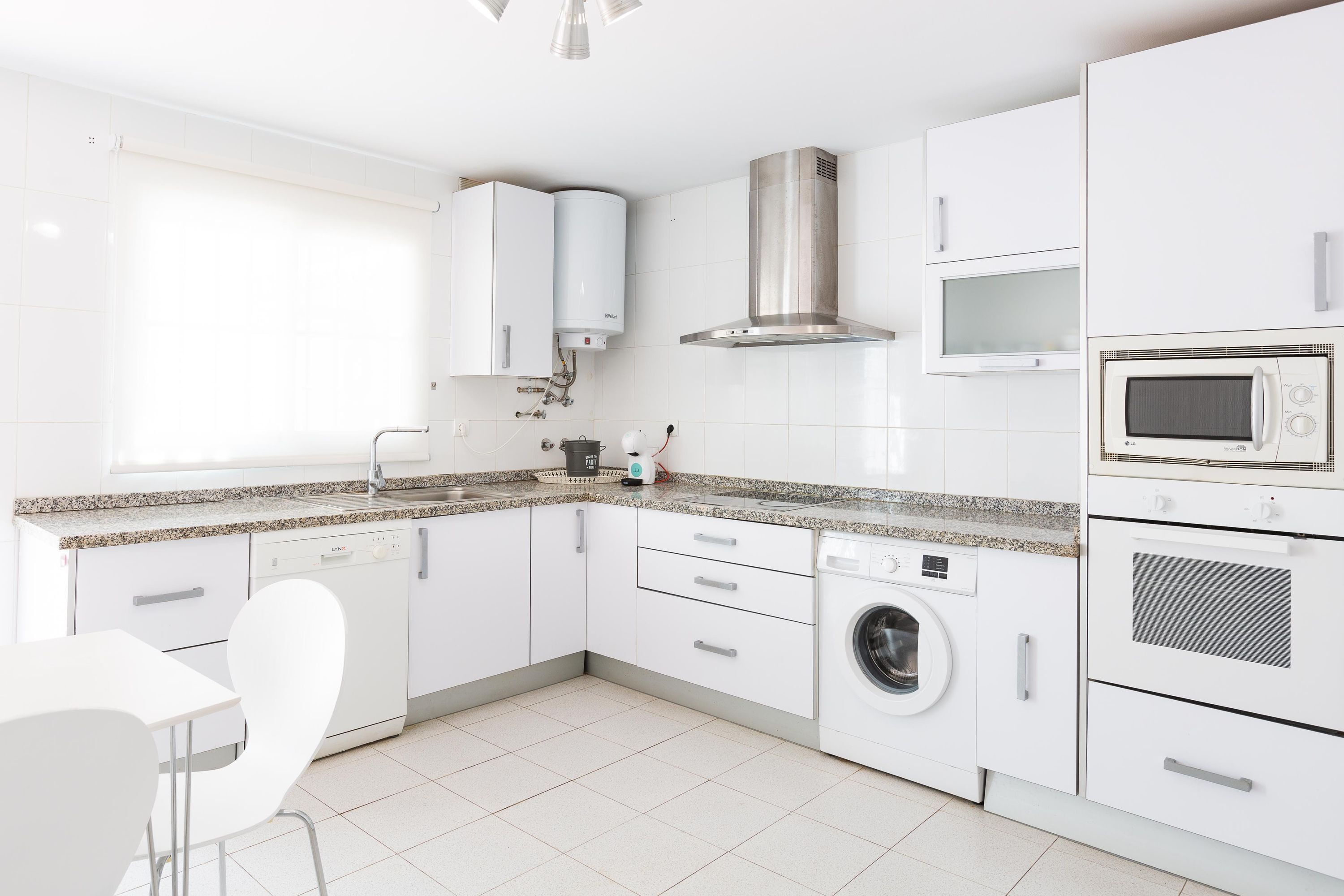 A modern kitchen with white cabinetry, a built-in washing machine, a microwave, and a stainless steel range hood.