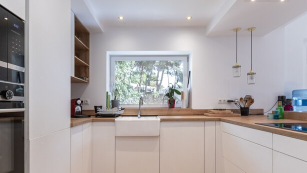 A modern kitchen with white cabinetry, a built-in oven, a window with a view of trees, and a countertop with various appliances and a sink. - Axarqu a in Malaga With 2 Bedrooms and 1 Bathrooms (Málaga)