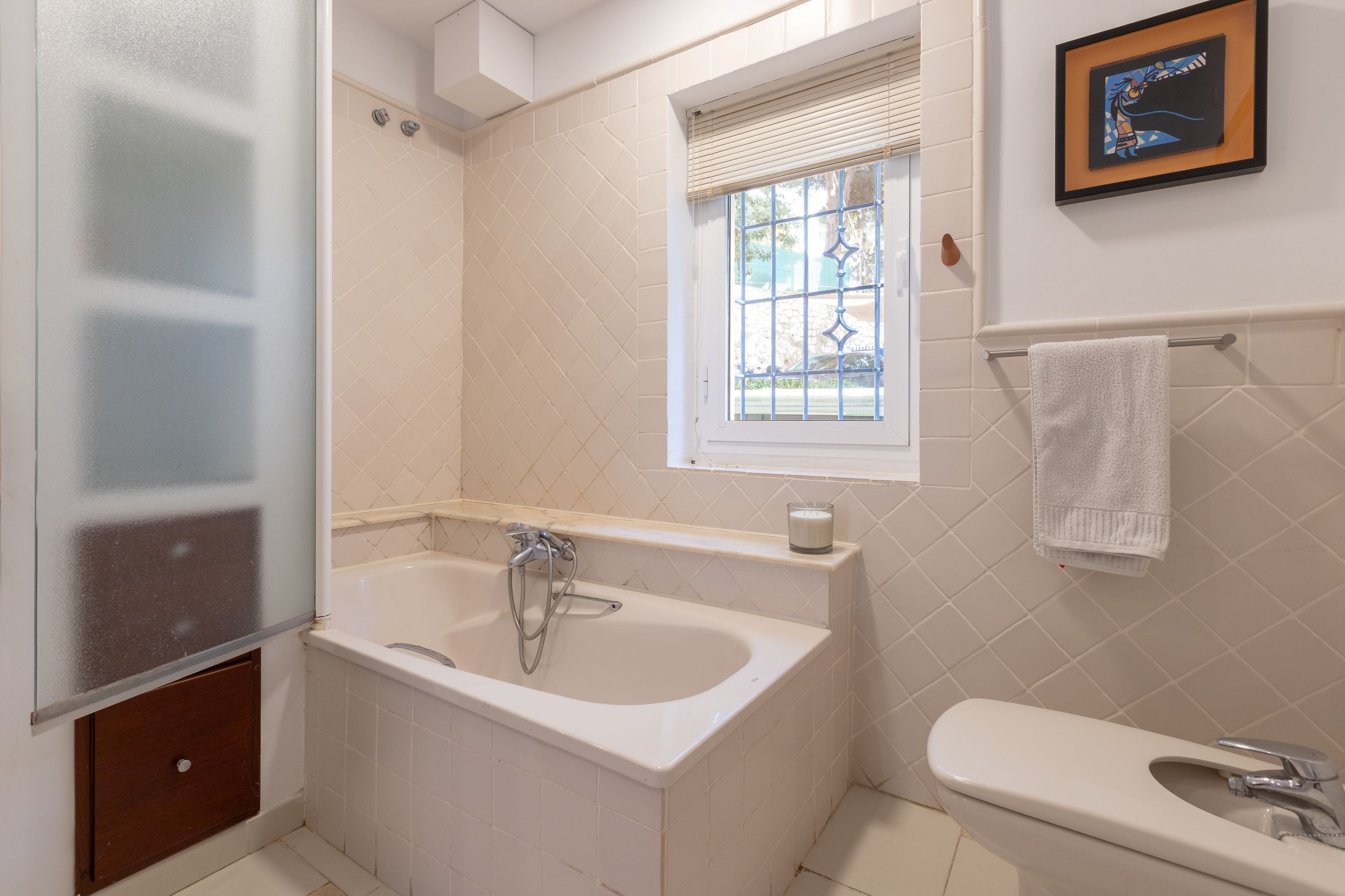 A bathroom with a bathtub, a sink, a window with blinds, and a towel rack.