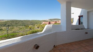 En balkon med en hvid væg og terracotta-fliser, der udover et grønt landskab og bygninger i det fjerne.
