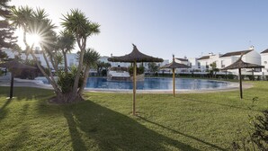A pool area with palm trees and thatched umbrellas, surrounded by white buildings. - Beautiful Duplex in Chiclana de la Frontera (Chiclana de la Frontera)