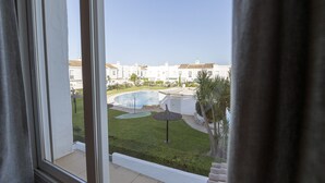 A view from a window overlooking a swimming pool, a grassy area, and white buildings. - Beautiful Duplex in Chiclana de la Frontera (Chiclana de la Frontera)