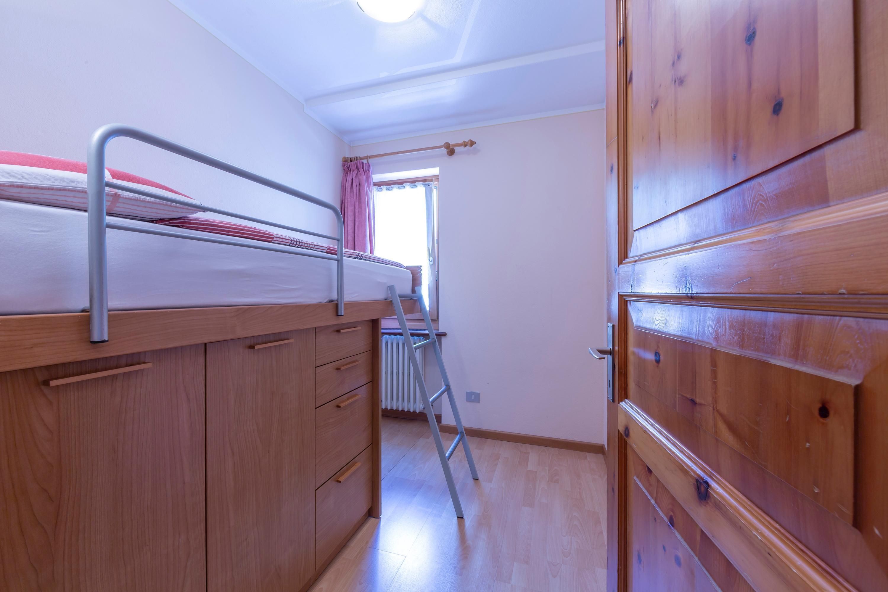 A bedroom with a bunk bed, wooden wardrobe, and a window with a curtain.