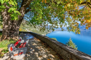 A bench with red accents, a stone wall, and a view of a lake and mountains. - Red View Apartment in Ronco Sopra Ascona Ascona (Ronco sopra Ascona)