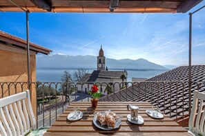A terrace with a table set for two, overlooking a mountainous landscape and a body of water. - Red View Apartment in Ronco Sopra Ascona Ascona (Ronco sopra Ascona)