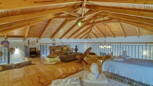 A spacious room with a high wooden ceiling, a bed with white linens, a wicker sofa with cushions, and a small table with a vase. - Villa John Dimeon With Private Pool (West Achaea)