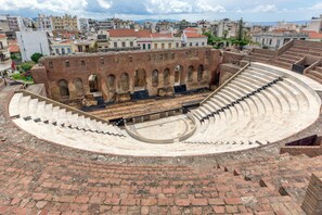An ancient amphitheater with a circular stage and tiered seating, surrounded by brick walls and a cityscape in the background. - Villa John Dimeon With Private Pool (West Achaea)