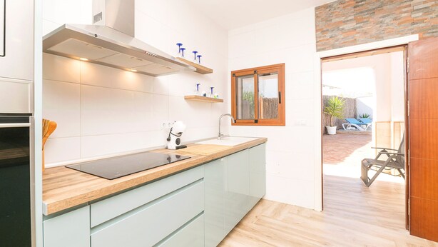 A modern kitchen with light blue cabinets, a wooden countertop, and a built-in stove. There is a window with a view of the outside. - Casa Azul in La Ribera de la Oliva (Barbate)