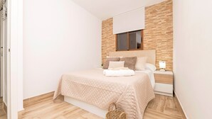 A bedroom with a bed, bedside table, lamp, and a wall-mounted window. - Casa Azul in La Ribera de la Oliva (Barbate)
