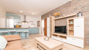A modern kitchen with a built-in oven and microwave, a dining area with a wooden table and bar stools, and a living room with a TV and wooden cabinets. - Casa Azul in La Ribera de la Oliva (Barbate)