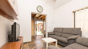 A living room with a sofa, a television, and a clock on the wall. - Casa Amelie in Conil de la Frontera (Conil de la Frontera)
