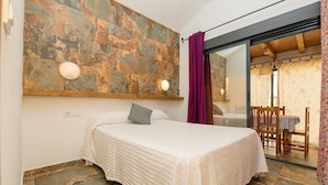 A bedroom with a bed, a stone wall, a wooden ceiling, and a view through a glass door. - Casa Amelie in Conil de la Frontera (Conil de la Frontera)
