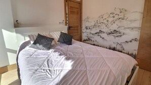 Een slaapkamer met een bed, twee kussens, een houten deur en een muurschildering van een berglandschap.