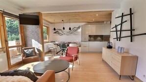 Een moderne woonkamer met een open haard, een eethoek en een keuken met houten kastjes en een zwart aanrecht.