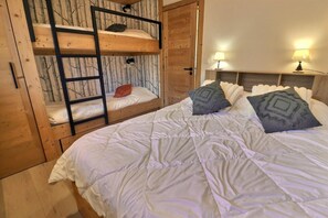 A room with a bunk bed, a single bed, and two bedside lamps.
