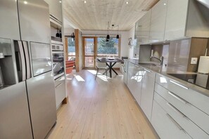 A modern kitchen with stainless steel appliances, wooden flooring, and a dining area with a table and chairs.