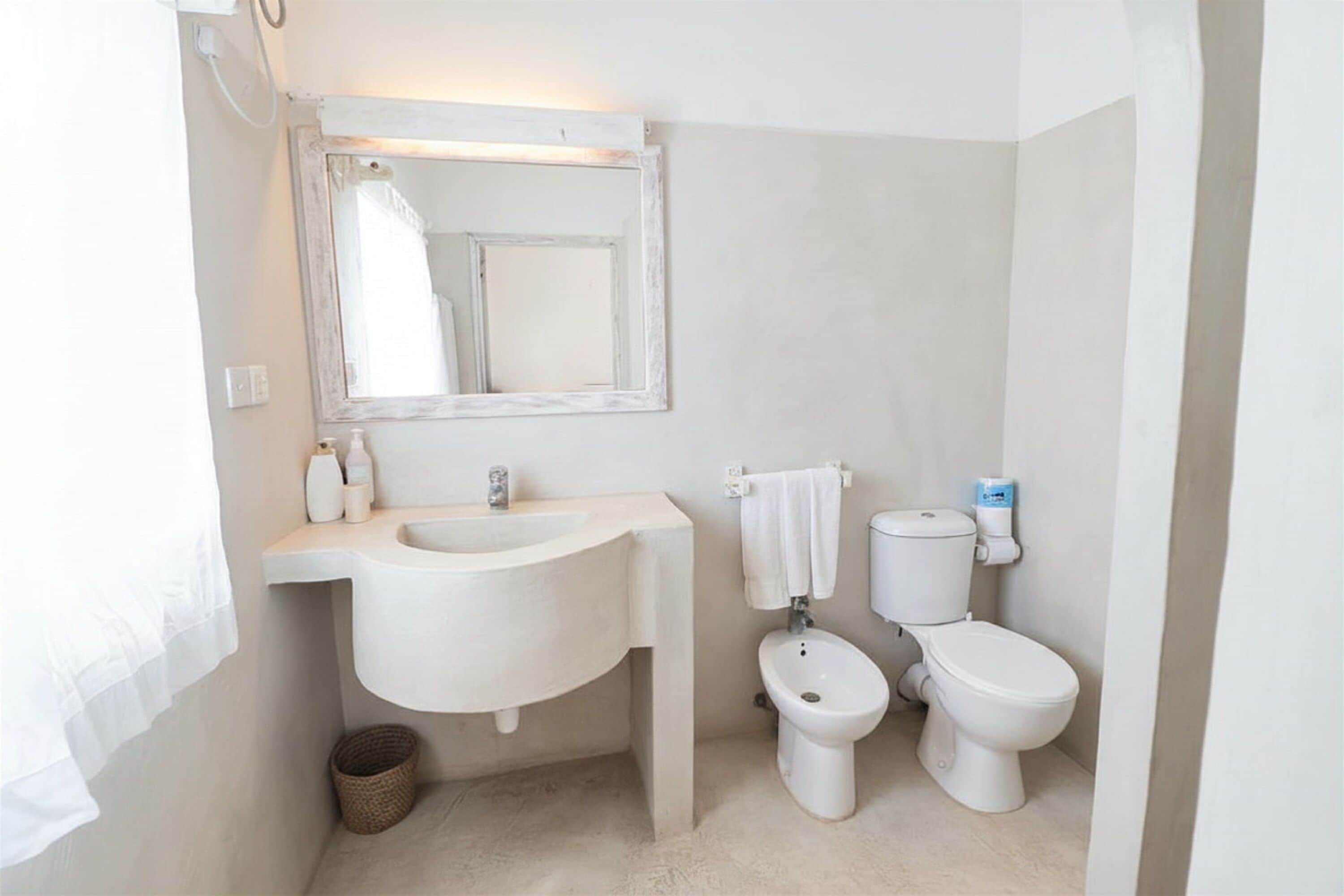 A bathroom with a sink, mirror, two toilets, and a towel rack.