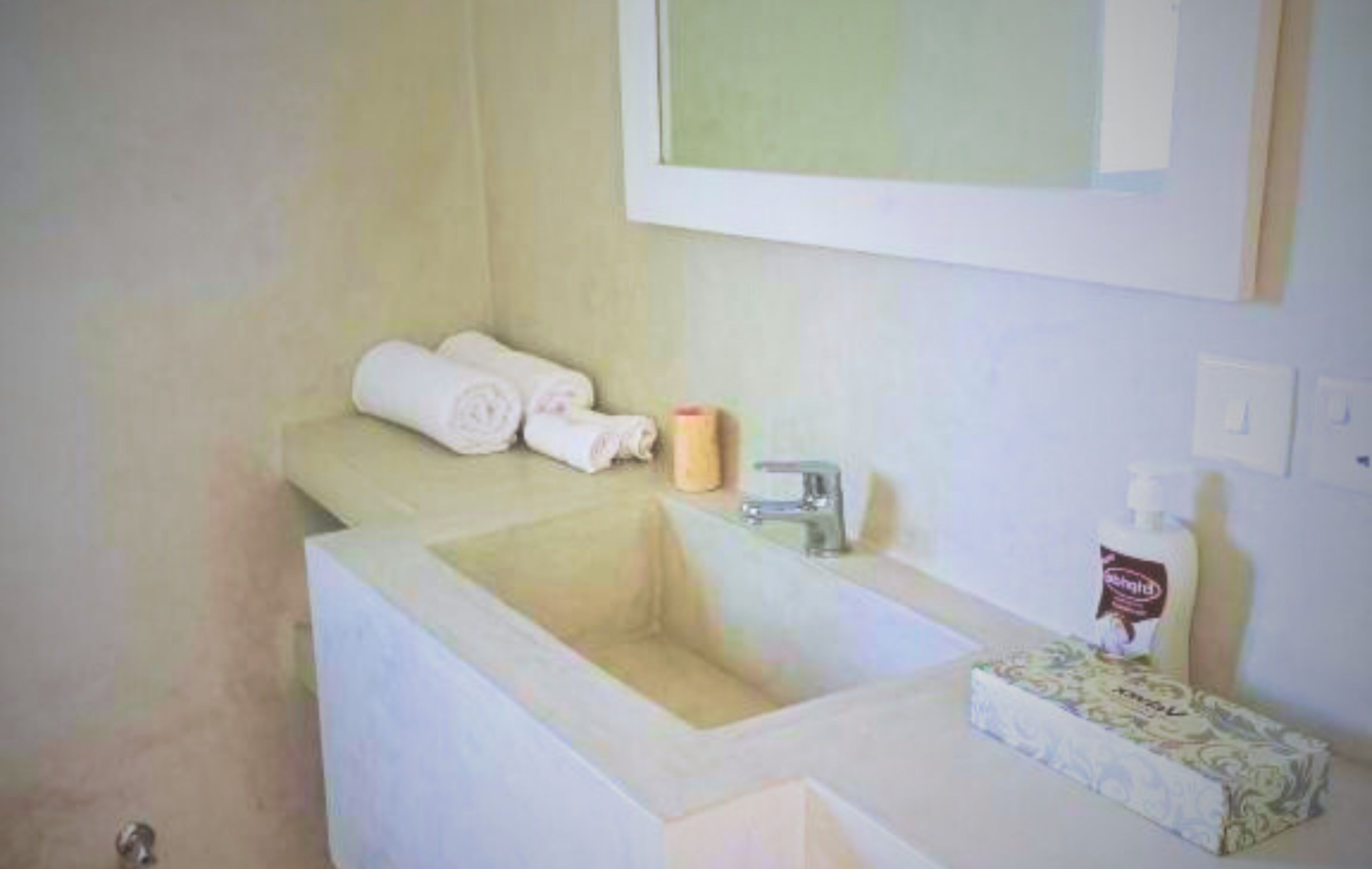 A bathroom with a sink, a mirror, a towel, and a box of tissues.