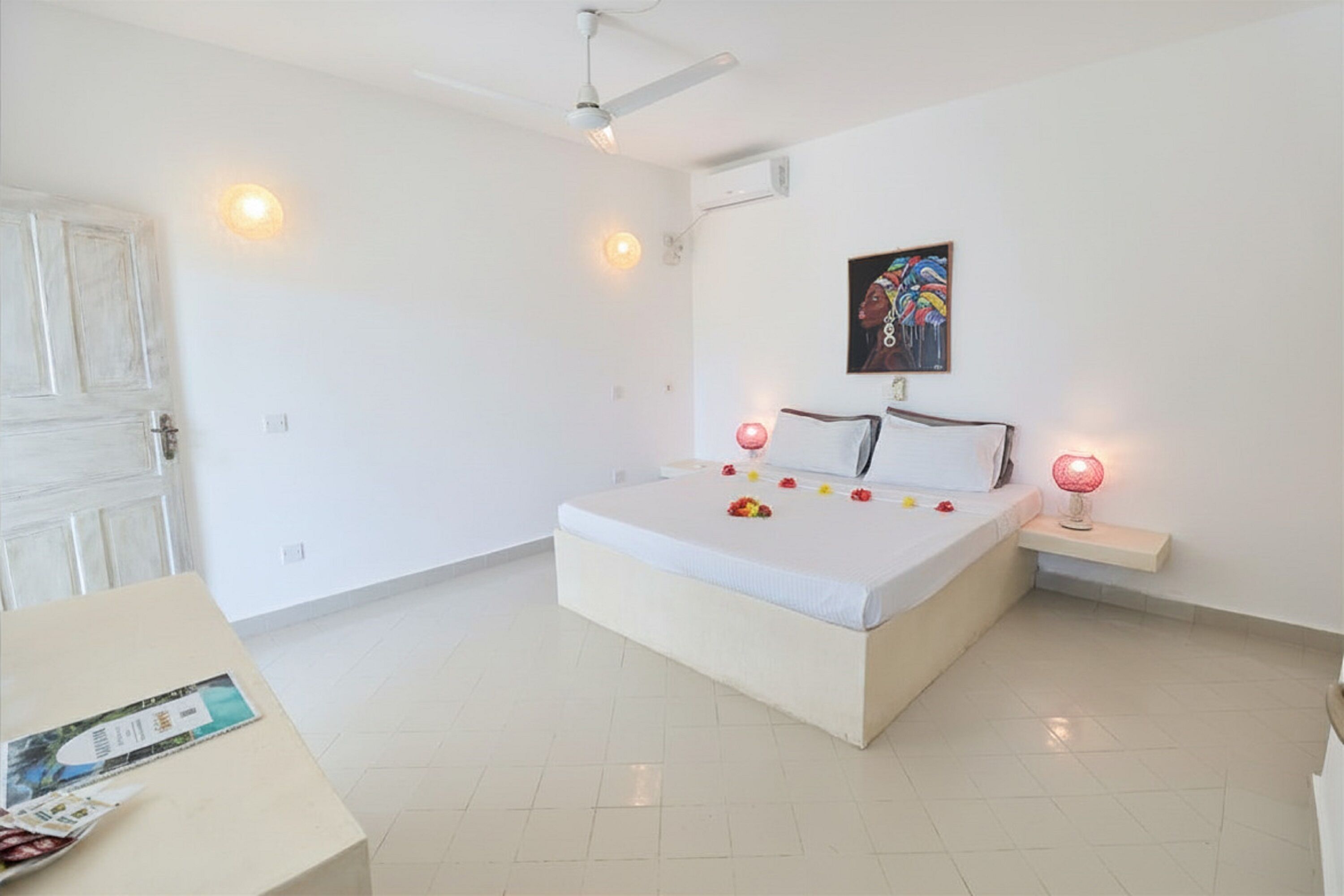 Un dormitorio con cama, lámparas de noche, ventilador de techo y un cuadro colgado en la pared.